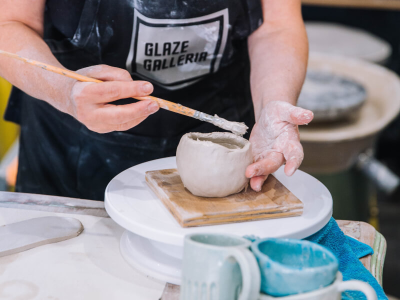A woman brushing clay at a pottery making class.